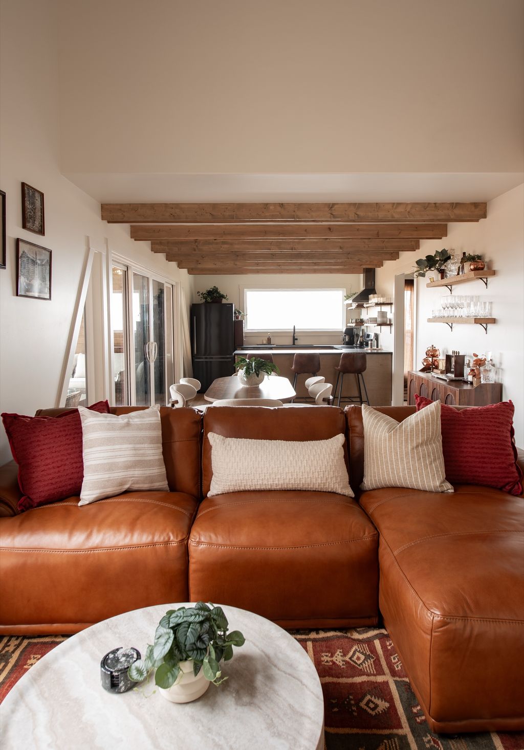Leather sectional and open living space with wood beams and kitchen beyond
